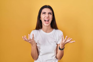 Sarı arka planda duran genç ve güzel bir kadın çılgın ve kızgın bir şekilde bağırıyor ve agresif bir ifade ve kollarla bağırıyor. hüsran kavramı. 