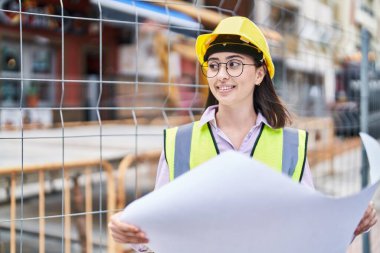 Young hispanic woman architect reading plans at street