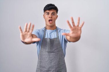 Beyaz arka plan üzerine önlük giymiş İspanyol genç adam avuç içi hareketlerini durduruyor, kızgın ve hayal kırıklığı ifadesi takınıyor. 