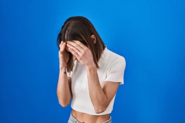 Mavi arka planda dikilen İspanyol kadın. Ağlarken yüzünü ellerle kapatan üzgün bir ifade. depresyon kavramı. 