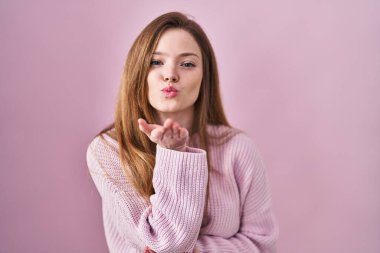 Pembe arka planda duran beyaz bir kadın kameraya bakıp havada bir öpücük savuruyor ve güzel ve seksi oluyor. aşk ifadesi. 