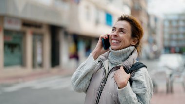 Orta yaşlı İspanyol kadın gülümsüyor. Akıllı telefondan konuşuyor.