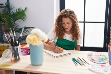 Young beautiful hispanic woman artist smiling confident drawing flowers pot on notebook at art studio