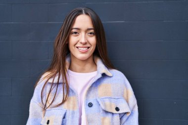 Genç, güzel İspanyol bir kadın, kendinden emin gülümsüyor, izole edilmiş siyah arka planda duruyor.