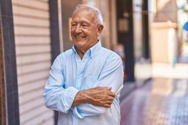 Senior grey-haired man smiling confident standing with arms crossed gesture at street
