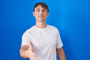 Beyaz, sarışın bir adam mavi arka planda durup dostça gülümseyerek selamlama ve hoş geldin diyor. başarılı iş. 