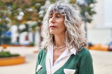 Parkta duran orta yaşlı, rahat yüzlü bir kadın.