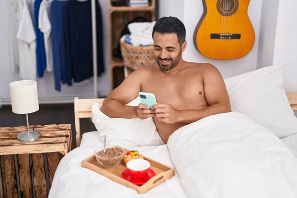 Young Hispanic Man Using Smartphone Having Breakfast Sitting Bed Bedroom — Stockfoto