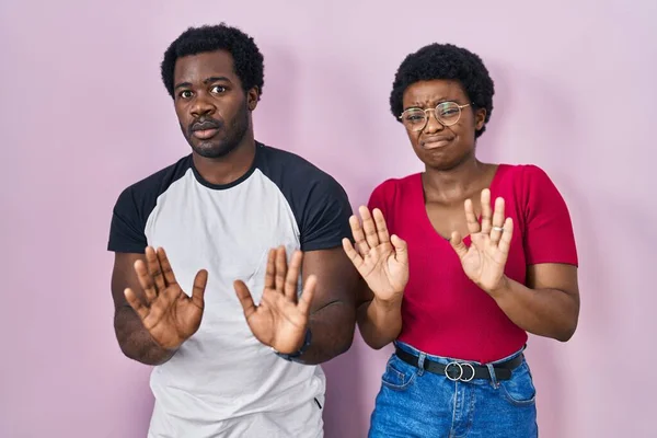 年轻的非洲裔美国夫妇站在粉红的背景上 手牵着手 带着恐惧和恶心的表情表示拒绝和否认 停止和禁止 — 图库照片