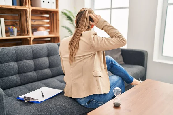 Young woman working at consultation office backwards thinking about doubt with hand on head