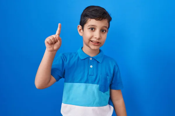 幸せな顔で指を指すアイデアや質問で笑顔で青い背景の上に立っている小さなヒスパニック系の少年 ナンバーワン — ストック写真