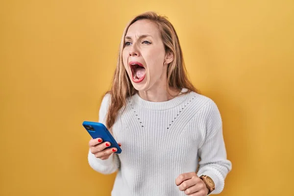 若いブロンドの女性は怒りで叫んで 怒りで叫んで 怒りと怒りを入力するスマートフォンのメッセージを使用しています 怒りと攻撃的な考え方 — ストック写真