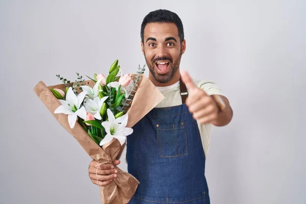 Hispanic man with beard working as florist approving doing positive gesture with hand, thumbs up smiling and happy for success. winner gesture.