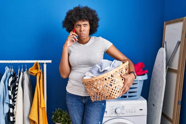 Black Woman Curly Hair Holding Laundry Basket Speaking Phone Skeptic — Fotografia de Stock