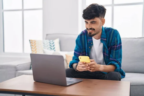 Young Hispanic Man Using Laptop Smartphone Sitting Sofa Home — Stockfoto