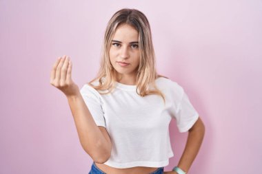 Pembe arka planda duran genç sarışın kadın italyan jestleri yapıyor. Elleri ve parmakları kendinden emin ifadesiyle. 