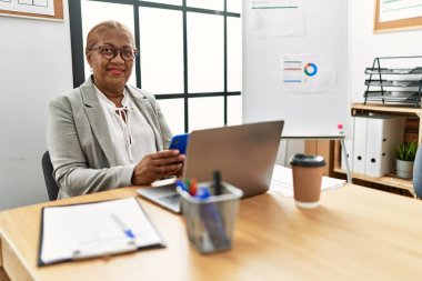 Kıdemli Afro-Amerikan kadın iş adamı. Ofiste çalışan akıllı telefonu kullanıyor.