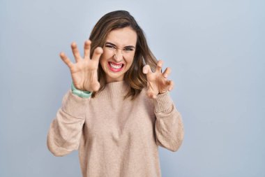 Soyutlanmış arka planda duran genç bir kadın komik bir şekilde kedi gibi pençe hareketi yapıyor, agresif ve seksi bir ifade. 