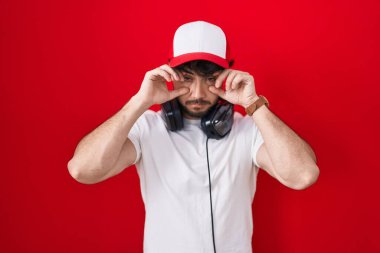 Oyun şapkası ve kulaklık takmış İspanyol bir adam parmaklarıyla gözlerini açmaya çalışıyor, uykulu ve yorgun bir şekilde sabah yorgunluğu çekiyor. 