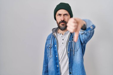 Dövmeleri olan, yün şapkalı, mutsuz görünen, reddedilmiş ve olumsuz jestli genç İspanyol bir adam. kötü ifade. 