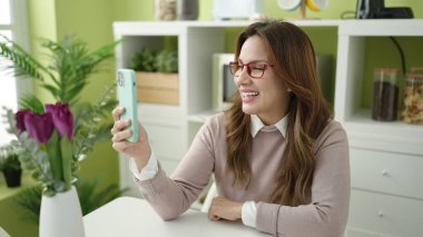 Genç, güzel, İspanyol bir kadın evdeki masada oturmuş video görüşmesi yapıyor.