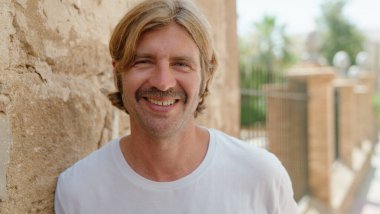 Sokakta kendine güvenen genç sarışın adam gülümsüyor.