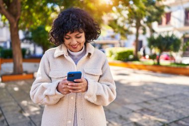 Parkta akıllı telefon kullanarak gülümseyen güzel bir İspanyol kadın.
