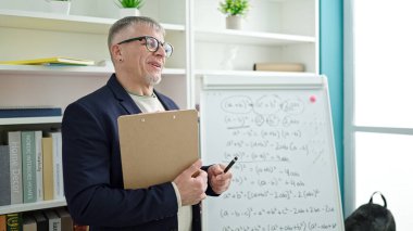 Orta yaşlı, kır saçlı erkek öğretmen üniversite sınıfında matematik dersi veriyor.