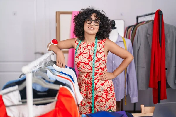 在裁缝店里 年轻的中东女性裁缝师自信地倚在衣架上微笑 — 图库照片