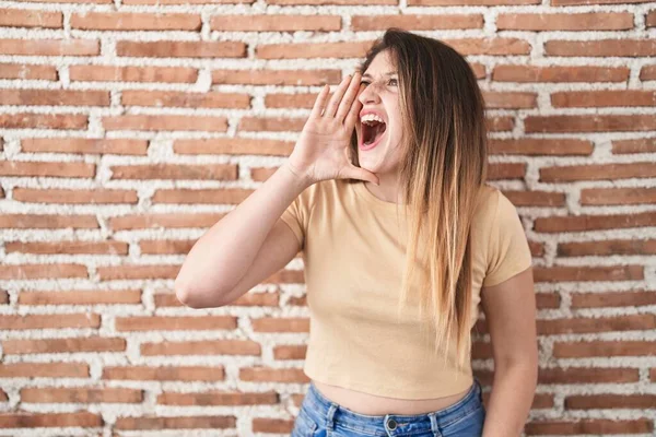 若いブルネットの女性がレンガの壁の上に立って大声で叫び 口の上に手で横に大声で叫ぶ コミュニケーションの概念 — ストック写真