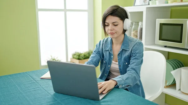 年轻的高加索女人坐在家里的桌子上 用笔记本电脑和耳机 — 图库照片