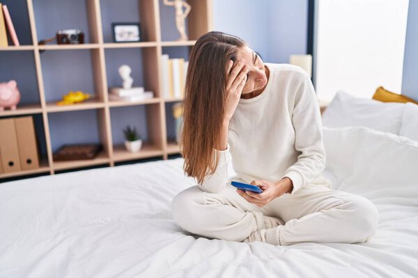 Young woman using smartphone with worried expression at bedroom