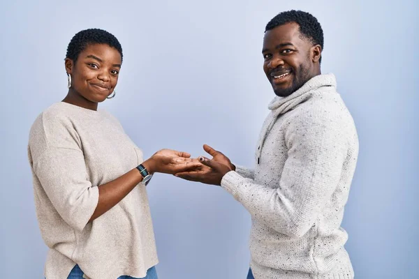 一对年轻的非洲裔美国夫妇站在蓝色的背景上 手拉着手掌 展示复制的空间 脸上挂着兴奋的广告微笑 — 图库照片