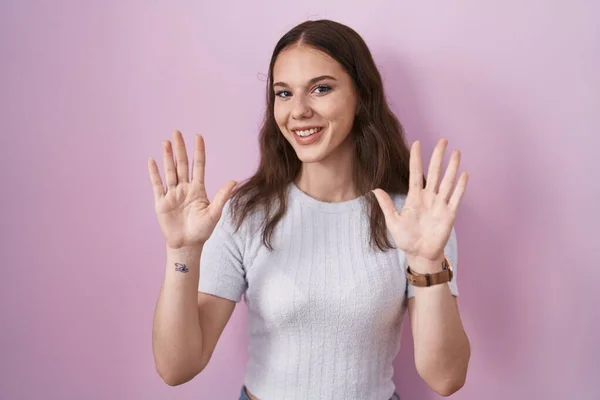 年轻的惊慌失措的女孩站在粉红的背景上 用十号手指指指着 自信而快乐地微笑着 — 图库照片