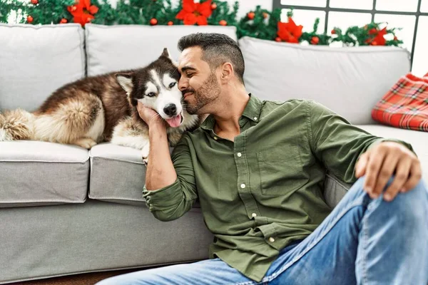Young Hispanic Man Kissing Dog Sitting Sofa Christmas Decor Home — стоковое фото