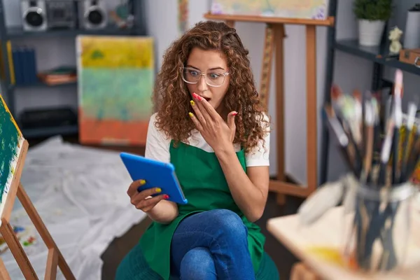 年轻的高加索妇女画家坐在艺术工作室里 用手捂住嘴 用平板电脑进行视频通话 感到震惊和害怕犯错 惊讶的表情 — 图库照片