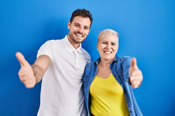 年轻的巴西母亲和儿子站在蓝色的背景上 看着镜头 张开双臂拥抱 欢快的表达拥抱幸福 — 图库照片