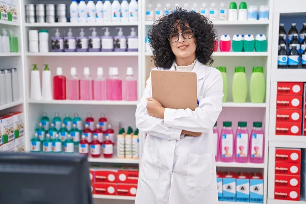 Young middle eastern woman pharmacist smiling confident holding clipboard at pharmacy
