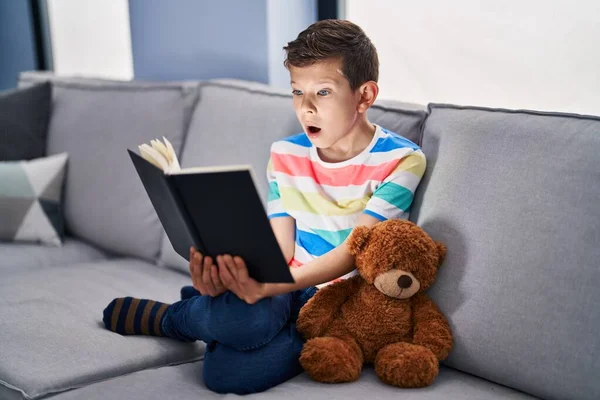 Niño Caucásico Joven Sentado Sofá Leyendo Libro Cara Choque Mirando —  Fotos de Stock