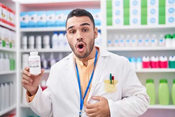 Young Hispanic Man Working Pharmacy Drugstore Holding Pills Scared Amazed — Stock Photo, Image