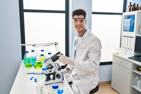 研究室で顕微鏡を使って科学者の制服を着た若いヒスパニック系の男 — ストック写真