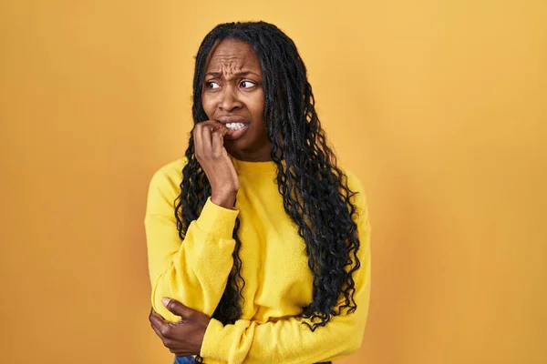 站在黄色背景上的非洲妇女看上去紧张而紧张 双手放在咬指甲的嘴上 焦虑问题 — 图库照片