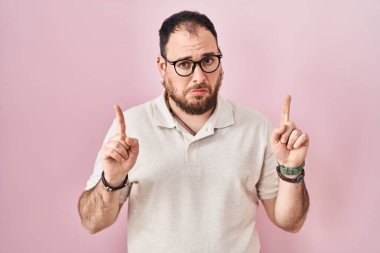 Ayrıca pembe arka planda duran sakallı, üzgün ve üzgün görünen, parmaklarıyla yön gösteren, mutsuz ve depresif İspanyol bir adam.. 