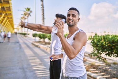 İki İspanyol erkek sportif çift gülümsüyor. Sokakta su içiyorlar.