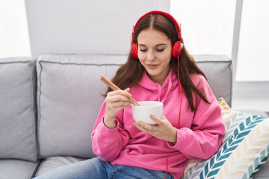 Young woman listening to music eating chinese food at home