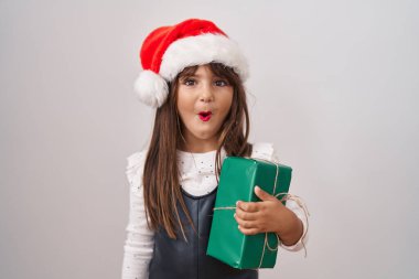 Küçük İspanyol kız noel şapkası takıyor ve elinde hediyeler var. Şaşırmış ve şaşırmış bir şekilde ağzı açık, inançsız bir yüz. 