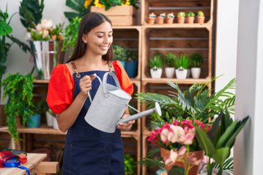 Young beautiful hispanic woman florist watering plant at florist