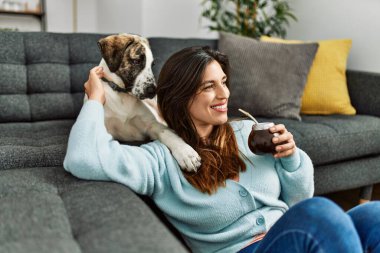 Young woman hugging dog drinking mate infusion at home