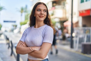 Kendine güvenen genç bir kadın caddede kollarını kavuşturmuş duruyor.