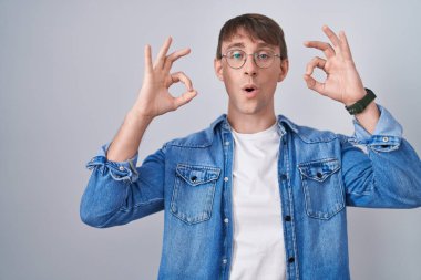 Beyaz, sarışın, gözlüklü, şaşırmış ve şoka uğramış bir adam. Onay sembolünü parmaklarıyla yapıyor. çılgın ifade 
